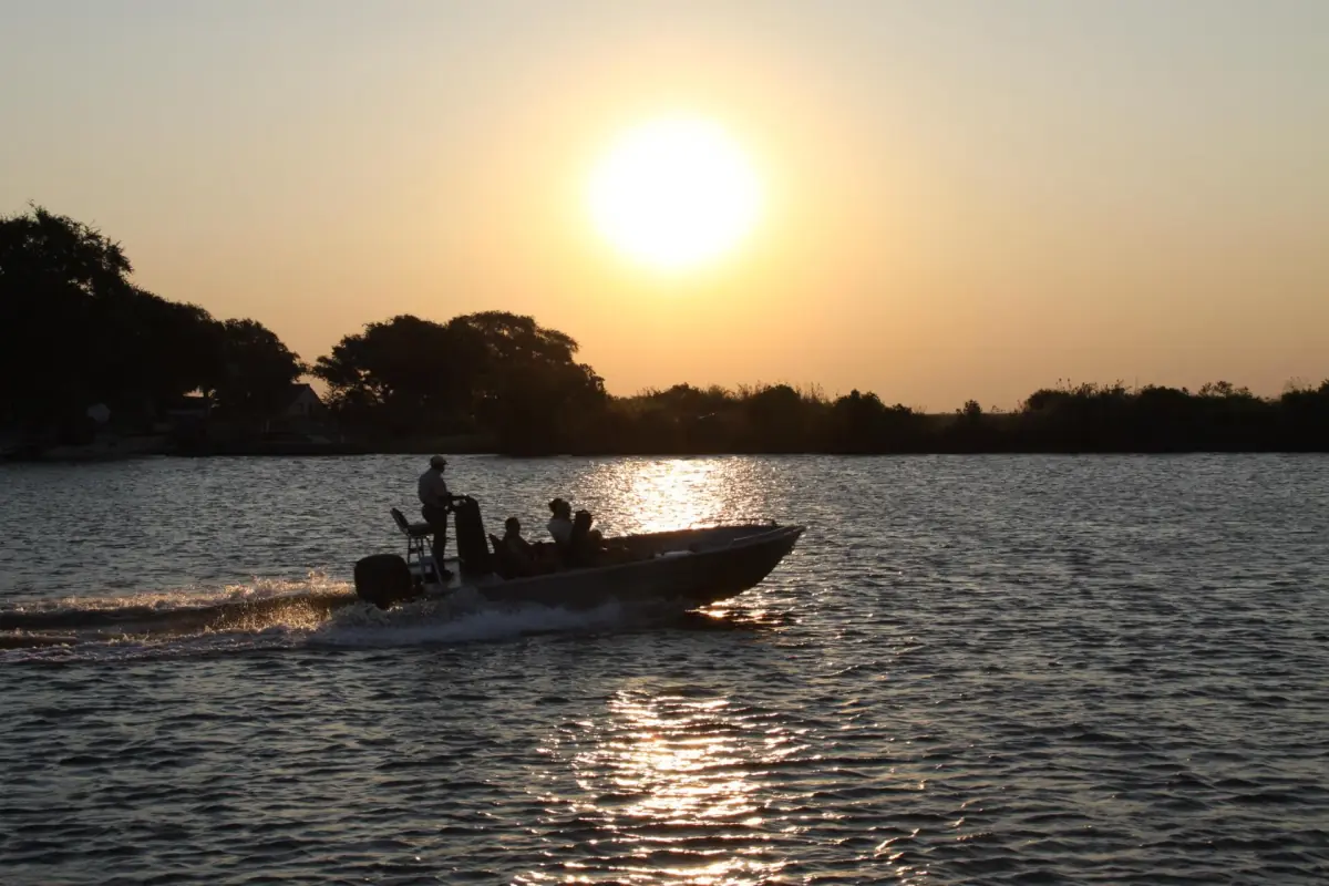A small boat on the Chobe River with the sun low over the trees